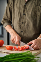 Unrecognizable young man cutting tomatoes at kitchen.