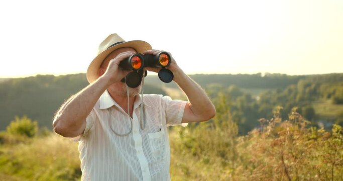 Senior man in a straw hat looking through binoculars