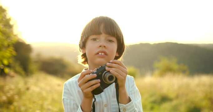 Little boy standing in a field with a camera at summer