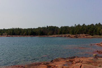 A quiet beach with some trees around it the sea is blue and the sky is like a sunny day there are some rocks around the beach everything looks peaceful and amazing to spend some time during summer