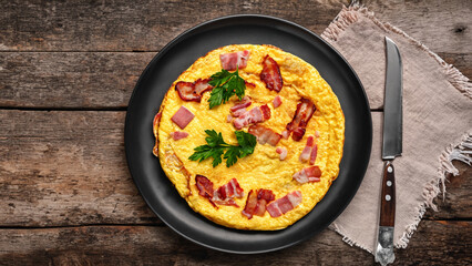 Obraz na płótnie Canvas Fried stuffed omelet. Tasty omelet with fried bacon and fresh parsley on a plate, fork, knife on old wooden background with copy space for text. Delicious egg breakfast. Vintage style. - generative ai