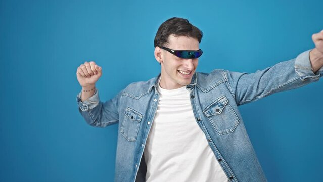 Young hispanic man using virtual reality glasses dancing over isolated blue background