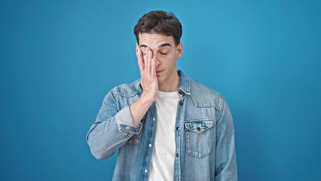 Young hispanic man stressed standing over isolated blue background