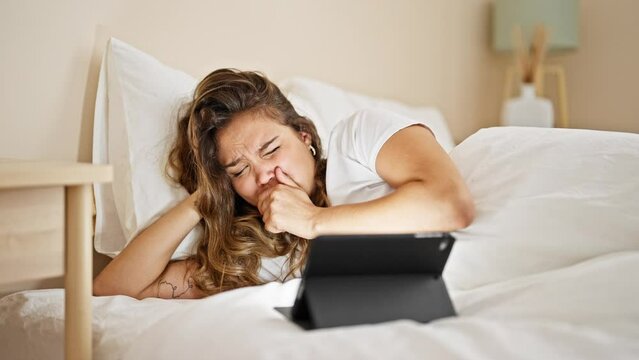 Young beautiful hispanic woman watching horror movie on touchpad lying on bed at bedroom