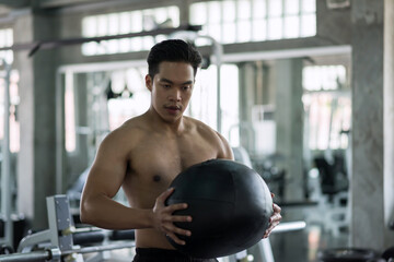 Asian strong muscle man training abdomen ball at gym