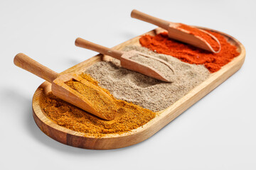 Wooden board with scoops of aromatic spices on light background