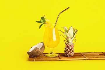 Glass of cocktail with baby pineapple and coconut on yellow background