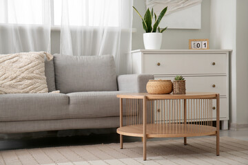 Wooden coffee table with with houseplant and wicker basket near grey sofa in living room