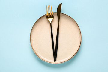 Table setting with clean plate and cutlery on blue background