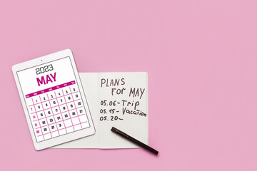 Modern tablet computer with calendar and notebook with plans for May on pink background