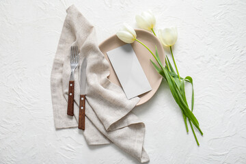 Clean plate with blank invitation card, cutlery and tulip flowers on white table