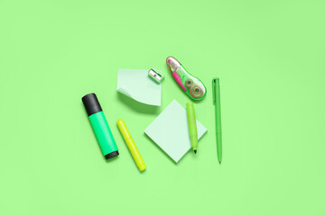 Sticky notes with different stationery supplies on green background