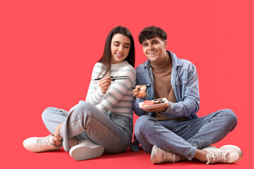 Young couple eating sushi on red background