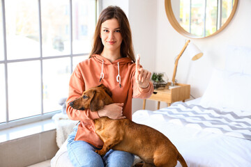 Young woman brushing teeth of her dachshund dog in bedroom