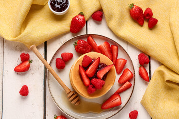 Plate with sweet pancakes, berries and jam on light wooden background