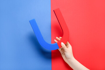Female hand with horseshoe shaped magnet on color background