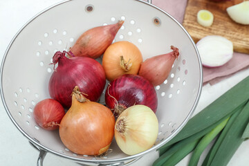 Wooden board and colander with different kinds of onion on white background