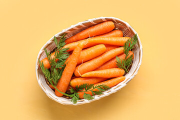 Wicker bowl with fresh carrots on orange background