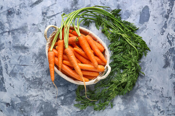 Wicker basket with fresh carrots on blue background