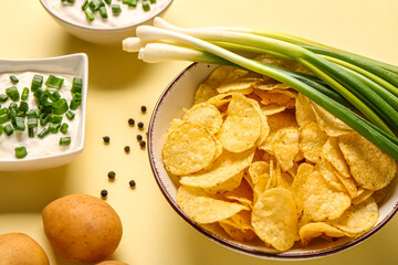 Bowls of tasty sour cream with sliced green onion and potato chips on yellow background