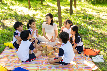 Cheerful school children picnicking outdoors with their teacher