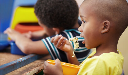 Child, lunch and eating in school, kindergarten or classroom and healthy nutrition, food and noodles. Kids, black boy and hungry kid or eat snack, pasta in lunchbox or breakfast in kindergarden