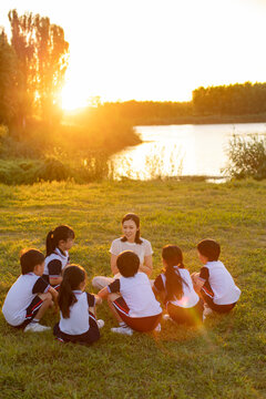 Cheerful school children relaxing in park with their teacher