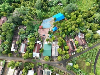 A stunning aerial view captured by a drone showing green trees and lush land with small buildings' rooftops in the frame.