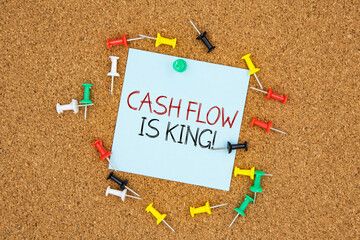 Cash flow is king text on light blue post-it paper pinned on bulletin cork board surrounding by...