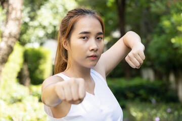 Young asian woman practicing kungfu qigong, martial arts, self defense technique in green urban park