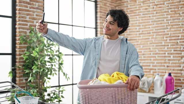 Young latin man make selfie by smartphone hanging clothes on clothesline at laundry room
