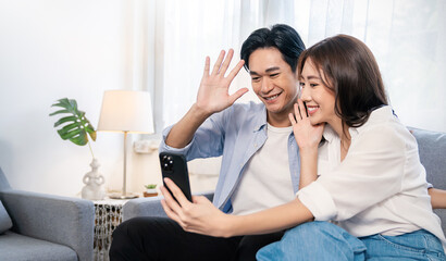 Portrait of asian parents couple use smartphone selfie say hi on sofa living room. Happy man woman online influencer blogger. Education technology connected people lifestyle concept