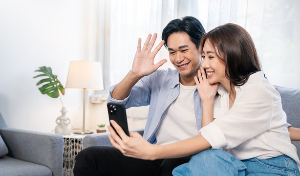Portrait of asian parents couple  use smartphone selfie say hi on sofa living room. Happy man woman online influencer blogger. Education technology connected people lifestyle concept