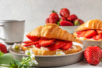 Croissant sandwiches with fresh ripe strawberries and cream cheese in a plate with cup of coffee for tasty breakfast