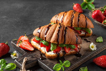Tasty breakfast. Croissants with strawberries, cream cheese, basil and chocolate sauce with flowers on dark background
