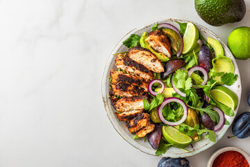 Grilled chicken fillet salad with arugula, avocado, plums, paprika, onion and lime in a plate on white background