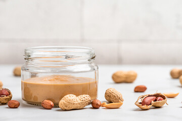Peanut butter jar and heap of nuts on white background. Organic vegan food. Tasty breakfast