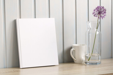 Mockup a paper book, an album with an empty cover and a white mug on a wooden table, the creator of the scene.
