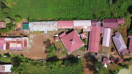 An impressive drone photo captured from an aerial view, showcasing the rooftops of buildings, red earth, and lush green trees in the surroundings.