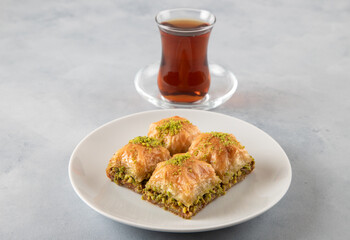 Pistachio baklava on a white plate with Turkish tea.A plate of traditional baklava on light blue background
