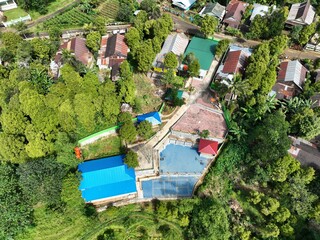 A stunning aerial view captured by a drone showing green trees and lush land with small buildings' rooftops in the frame.