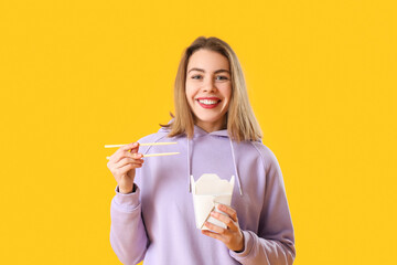 Young woman with box of Chinese noodles on yellow background