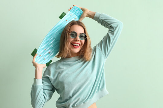 Young woman in sunglasses with skateboard on green background