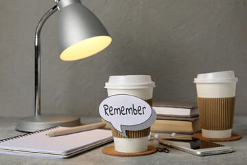 Cup of coffee with reminder, mobile phone, notebooks and glowing lamp on grunge table, closeup