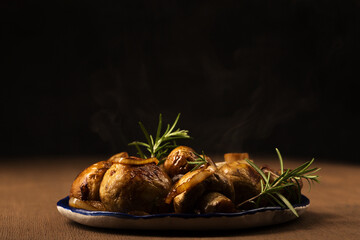 Fried mushrooms champignons with rosemary and onions on a plate on a dark