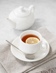 Tea with lemon in a white cup on a light background with  a teapot. The concept of a healthy and...