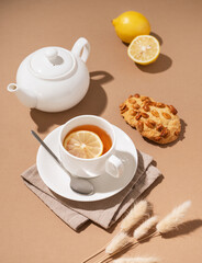 Creative layout of a cup of herbal tea with cookies, lemon and teapot on a brown background with a...