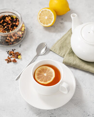 A cup of herbal tea with lemon and teapot on a light  background close up. Healthy and detox  drink concept for breakfast.