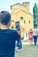 Boy enjoying the  view  of Saint Stephen church at  Bologna . Concept of traveling famous landmarks in Italy. Caucasian  Boy tourist   making a photo with a phone 