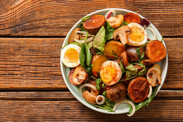 Plate of tasty potato salad with eggs and mushrooms on wooden background, top view